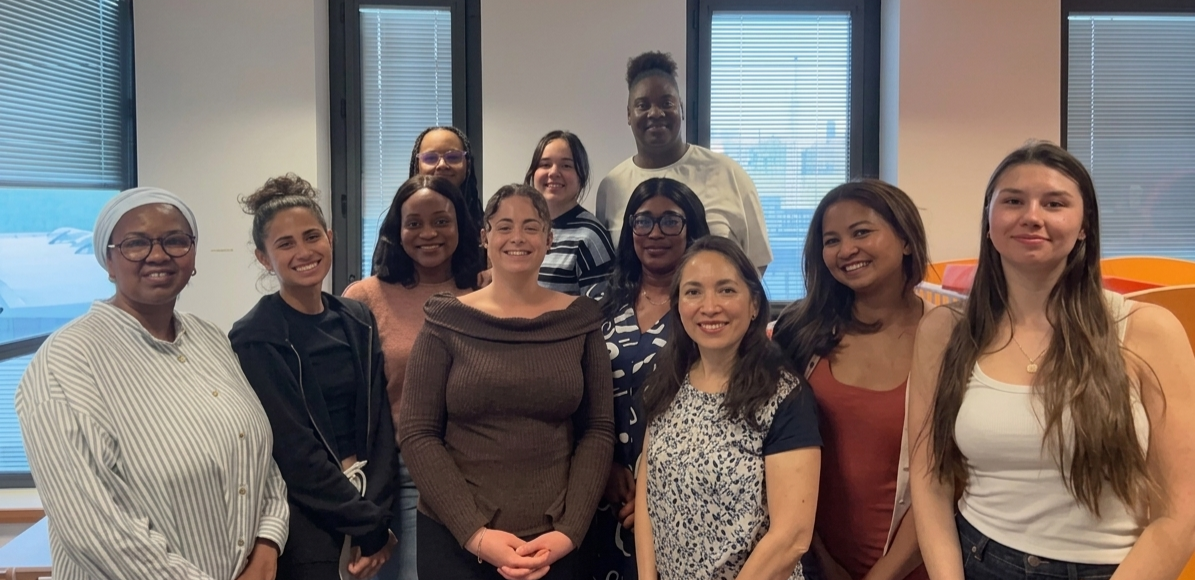 Diverse group of coworkers posing for a team photo in a bright office, smiling at the camera near large windows.