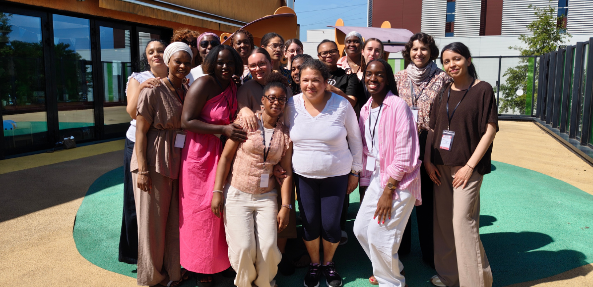 Group of about 20 diverse women posing together outdoors, smiling, with lanyards and badges.