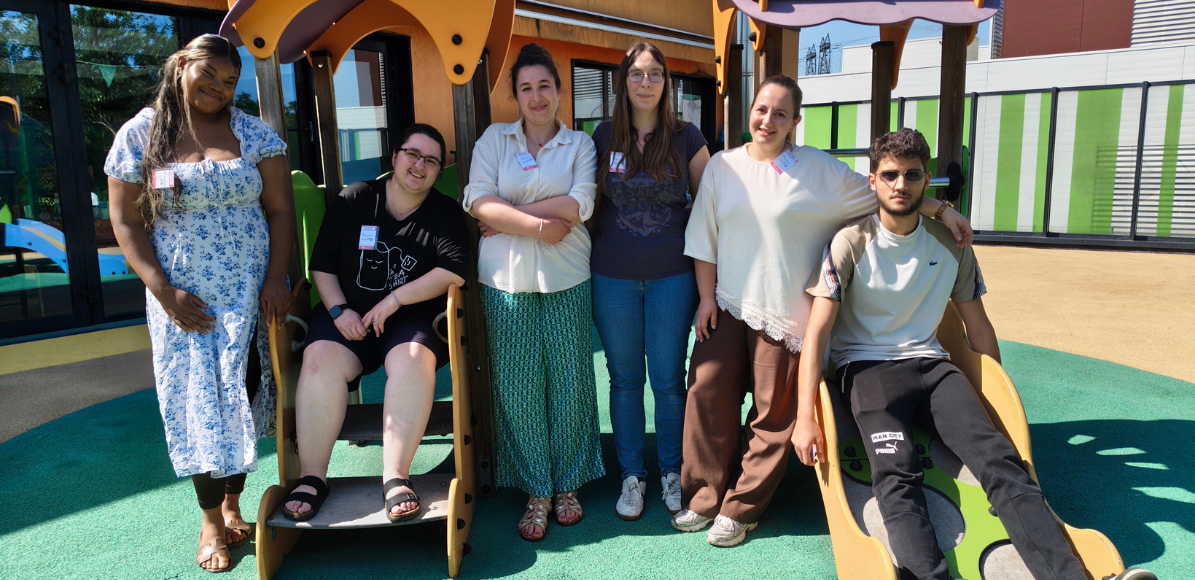 Seven people posing together on a playground structure outdoors, smiling at the camera.