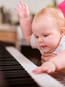 Baby reaching and pressing piano keys while held for support, exploring the instrument.