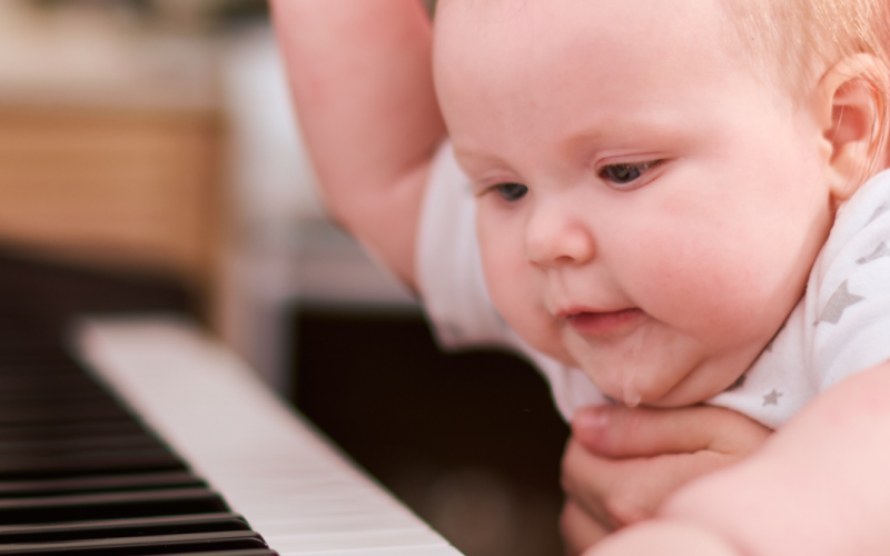 Baby reaching and pressing piano keys while held for support, exploring the instrument.